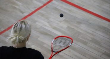 Squash player strikes ball during singles league match.