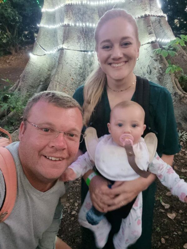 A portrait photo of a man, woman and a baby taken outside in a garden setting.