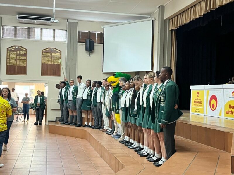 A group of high school children and a mascot dressed as a falcon standing in a line infront of the school hall on steps.