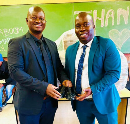 An image of primary school principals Mr Dlamini and Mr Zakhele Xulu display school shoes donated to learners by an NPO.