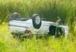 Image of a white car on its roof in a grass field.