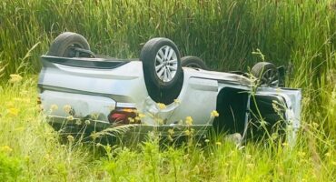 Image of a white car on its roof in a grass field.