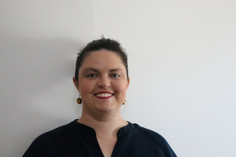 A woman who works at the Newcastle Advertiser dressed in their formal black uniform in front of a white background.