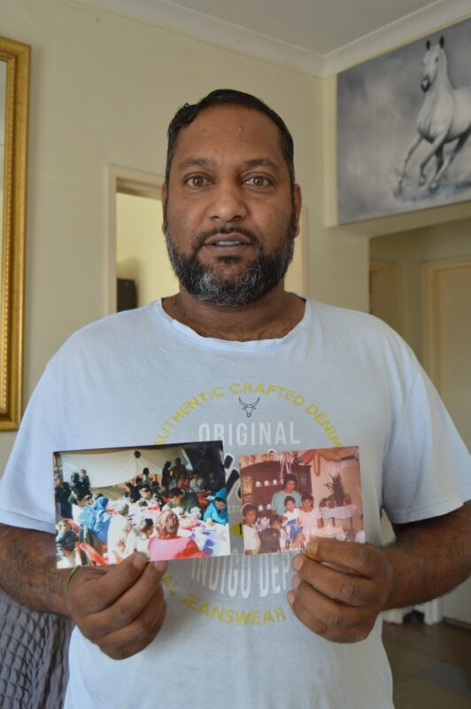 A man is pictured standing in his home, holding two photos of loving memories.