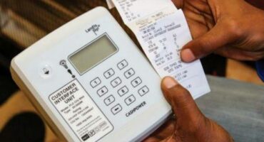 Image of hands typing in on a prepaid meter with the token in the other hand.