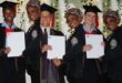 A collage of three students and a teacher holding academic certificates. All three students have graduation hats on their heads and they are wearing school blazers. The teacher is wearing a school blazer too, with a headscarf on her head. There are fairy lights and greenery in the background.