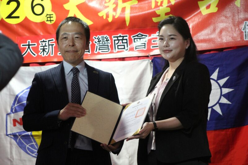 Two people are photographed in front of a red, gold and yellow Chinese New Year banner during the Taiwanese New Year Celebrations.