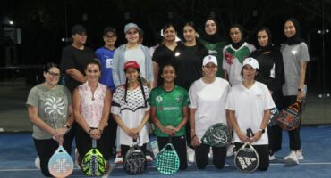A group of women pose inside a padel court at night.