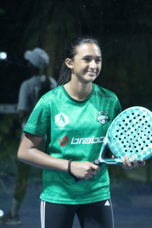 A female padel player with her padel racquet in side the padel court at night.