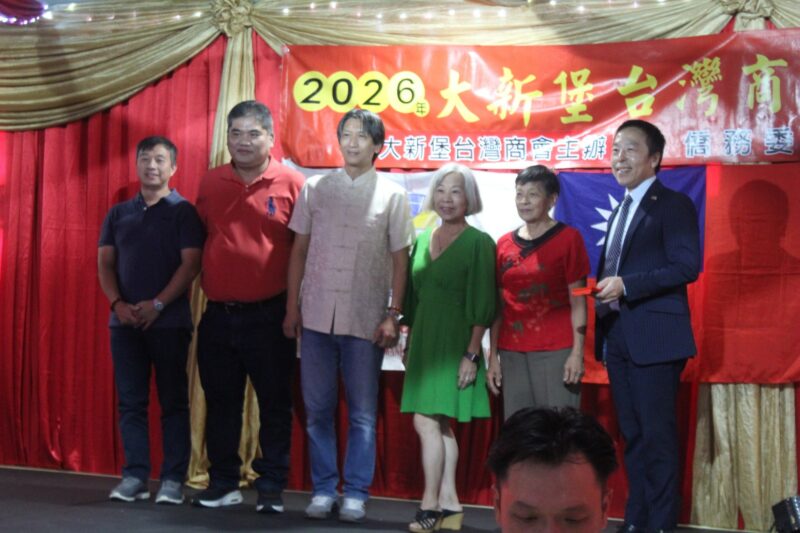 A group of people are photographed in front of a red, gold and yellow Chinese New Year banner during the Taiwanese New Year Celebrations.