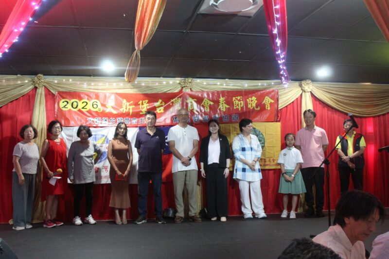 A group of people are photographed in front of a red, gold and yellow Chinese New Year banner during the Taiwanese New Year Celebrations.