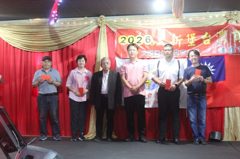 A group of people are photographed in front of a red, gold and yellow Chinese New Year banner during the Taiwanese New Year Celebrations.