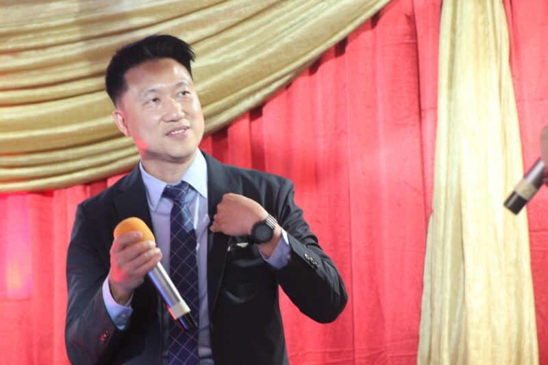 A photo of a man standing in front of a red and gold draping celebrating the Taiwanese New Year.