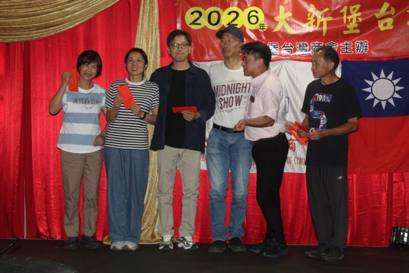 A group of people are photographed in front of a red, gold and yellow Chinese New Year banner during the Taiwanese New Year Celebrations.