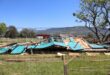 A collapsed classroom at Utrecht Primary School. The classroom is now behind a fence to secure further damages and or loss of property. The classroom was a turqoise colour. It is a very bright day, with mountains in the bachground. The sky is a deep blue.