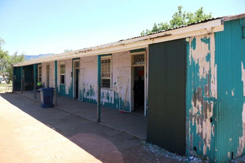 A 90 year old train shed at Utrecht Primary School. The paint is peeling off. The doors and windows are open. The shed is rectangular in shape.
