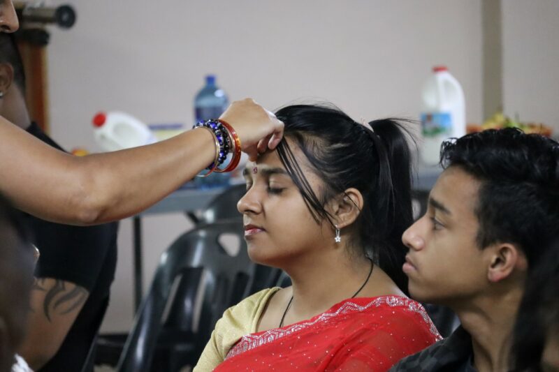 A woman applies a red tilak to a devotee’s forehead during a temple ceremony.