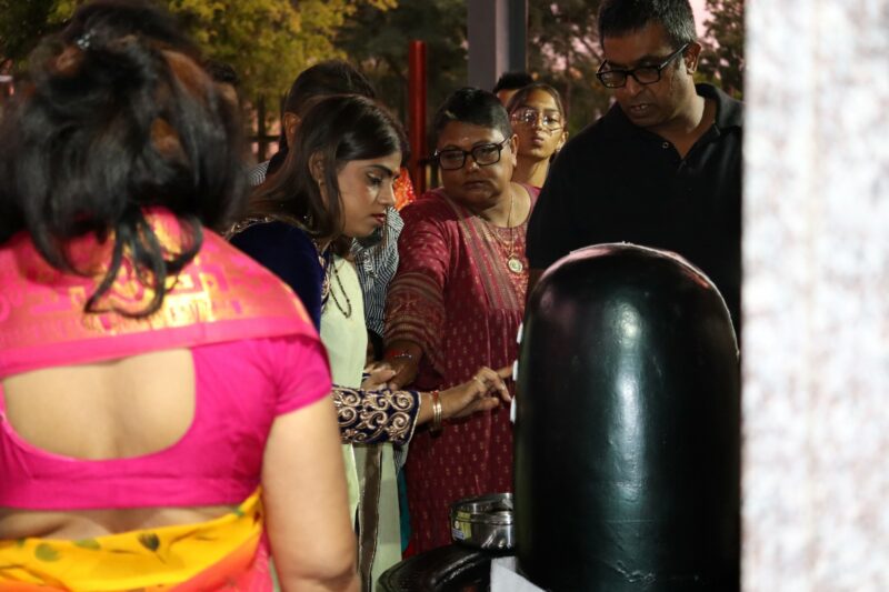 Devotees remained awake through the night, offering milk, sour milk, water, ghee and bilva leaves to the Shivalinga. These devotees are outside; it is night time. One devotee is smeering something on the Shivalinga, while others look on.