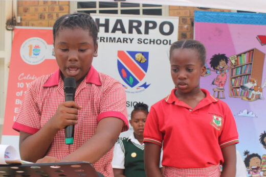 An image of two learners from Besterspruit Primary School, one of them holding a micro-phone to read aloud in both English and IsiZulu.