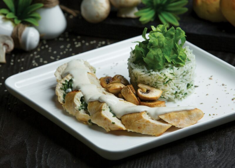 A plate with Marry me chicken and rice with herbs on a white plate on a dark table setting.