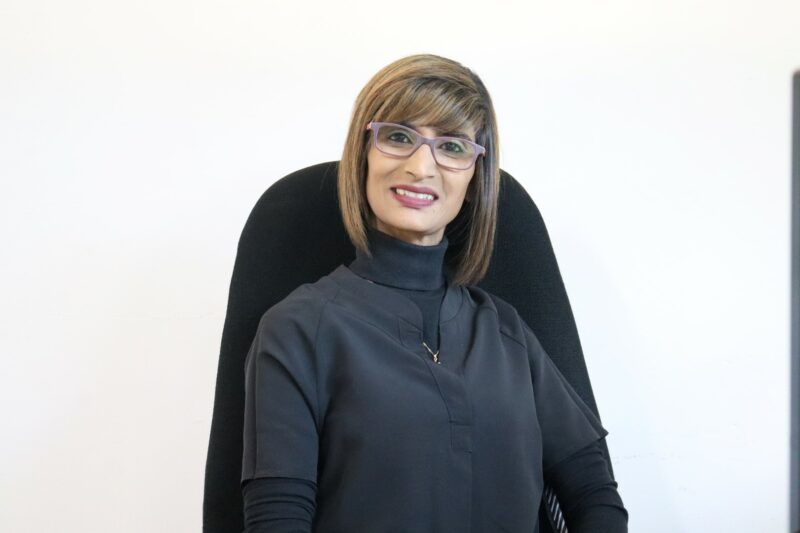 A woman who works at the Newcastle Advertiser dressed in their formal black uniform in front of a white background.