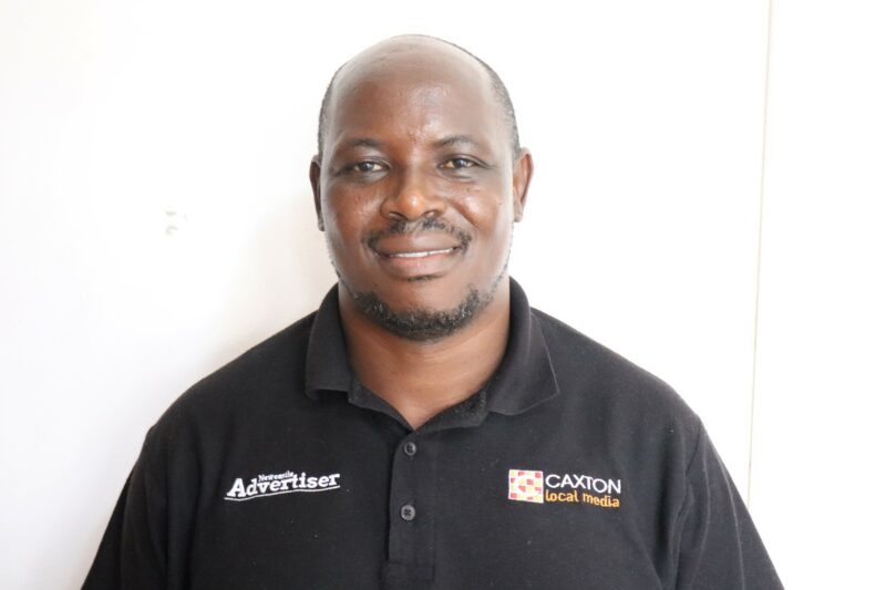 A man who works at the Newcastle Advertiser dressed in their formal black uniform in front of a white background.