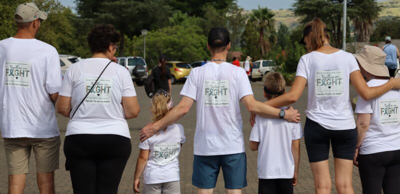 Two families with white t-shirts on. The printing at the back is saying "Brain cancer fighter." The little boy without the printing on his shirt is the one who survived the brain cancer. They are all turned with their backs to the camera as the finished the walk together.