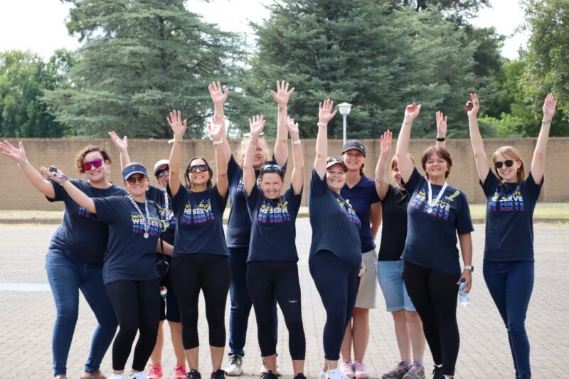 Members from the Newcastle Lions Club with their hands in the air after a successful event. The are all wearing blue t-shirts with multi-coloured writing on it.