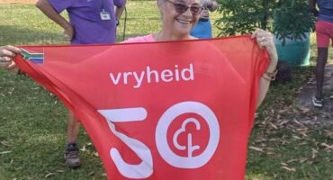 Image of an elderly lady holding Vryheid parkrun's red flag with a 50 on it.