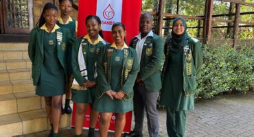Image of learners from VHS dressed in school uniform standing in front of a SANBS banner.