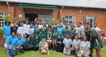Image of learners from Vryheid High School dressed in dark green and yellow school uniforms in front of old age home.