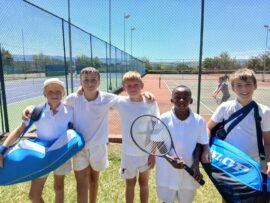 A group of young tennis players posing in front of the tennis courts.