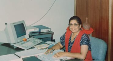 A woman is photographed sitting behind a desk in an office setting.