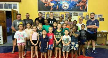 Image of group of young wrestlers and coaches standing in front of the Vryheid Wrestling Club banner.