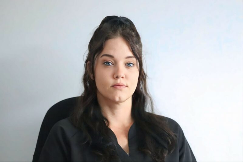 A woman who works at the Newcastle Advertiser dressed in their formal black uniform in front of a white background.