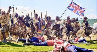 Image of the re-enactment of the battle of Isandlwana with Zulu warriors and British redcoats depicted.