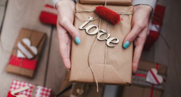 Hands holding a wrapped Valentine’s gift with wooden “love” decoration.