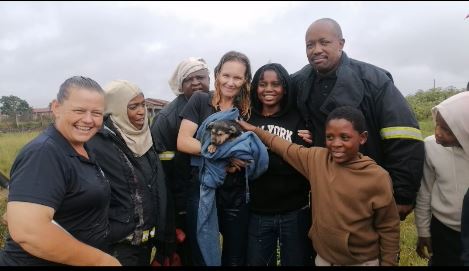 A group of people posing in the rain with a puppy rescued from a drainpipe.