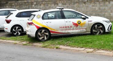 Three white vehicles parked on grassy sidewalk next to a road.