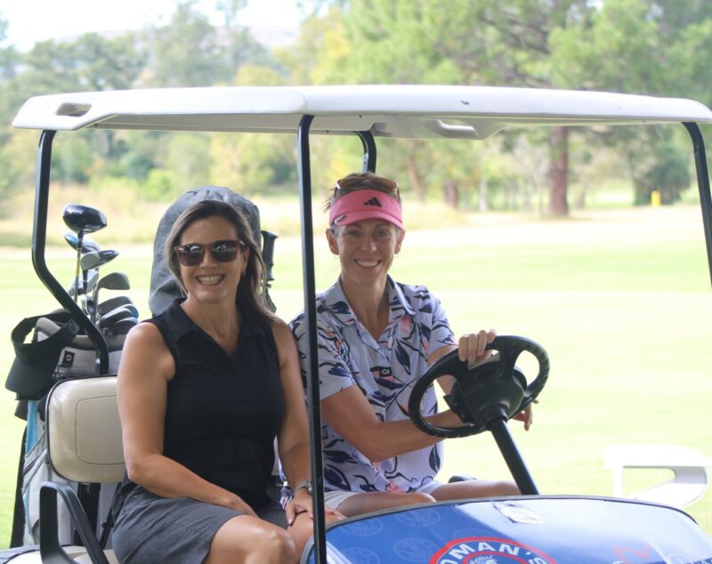 Two golfers posing for a photo in a golf cart at the Newcastle Golf Club.