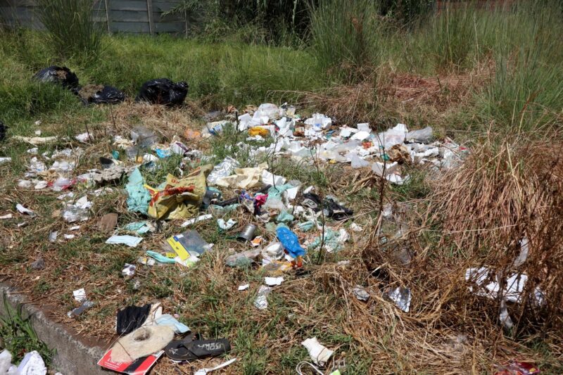 Dumped rubbish scattered in overgrown field near Voortrekker Street.