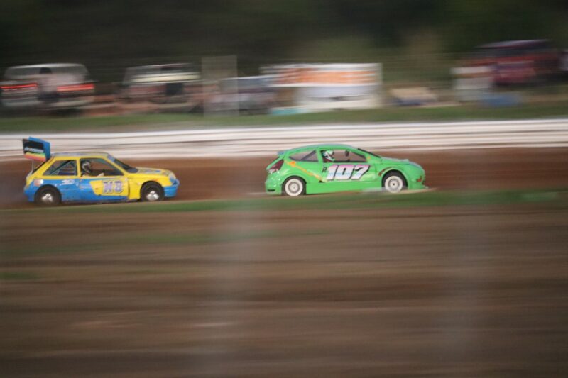 Two cars are racing against each other at the oval track.