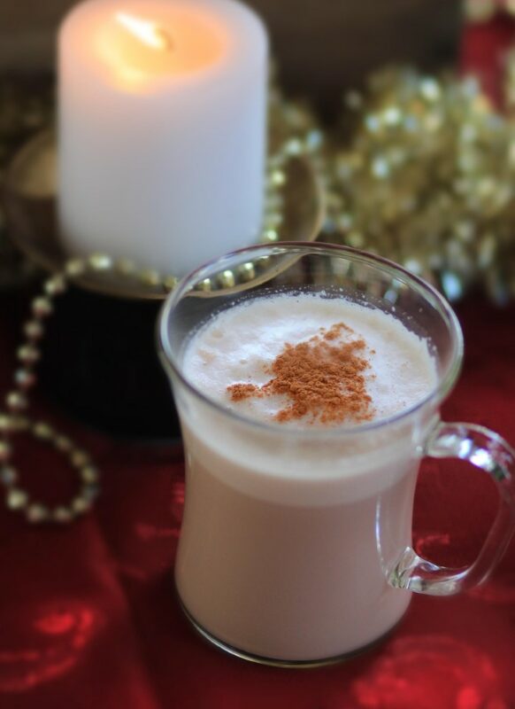 Chai tea with cinnemon and foam on top. The tea is in a big glass cup. There are pearls and a candle in the background.