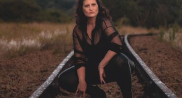 Image of a woman dressed in black while crouches on a train track for a photoshoot.