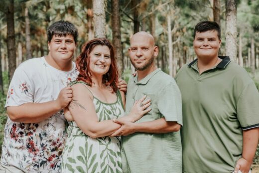 Image of a woman, a man and two teenage boys all dressed in sage green standing in a 'forest'.