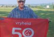 Image of elderly man with a cap and blue shirt holding a red banner with 50 parkrun.