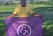 Image of a man in yellow shirt holding a purple parkrun flag with 25 volunteer on it.