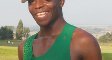 Image of a runner with a white cap and green shirt and a huge smile.