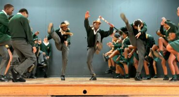 Image of learners performing traditional Zulu dances on stage in school uniform.