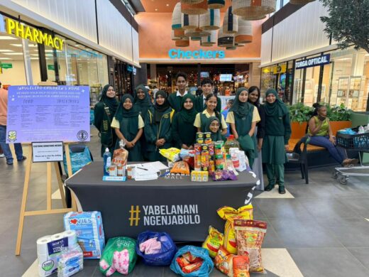 Learners in green and yellow uniforms standing in a mall with donated groceries.